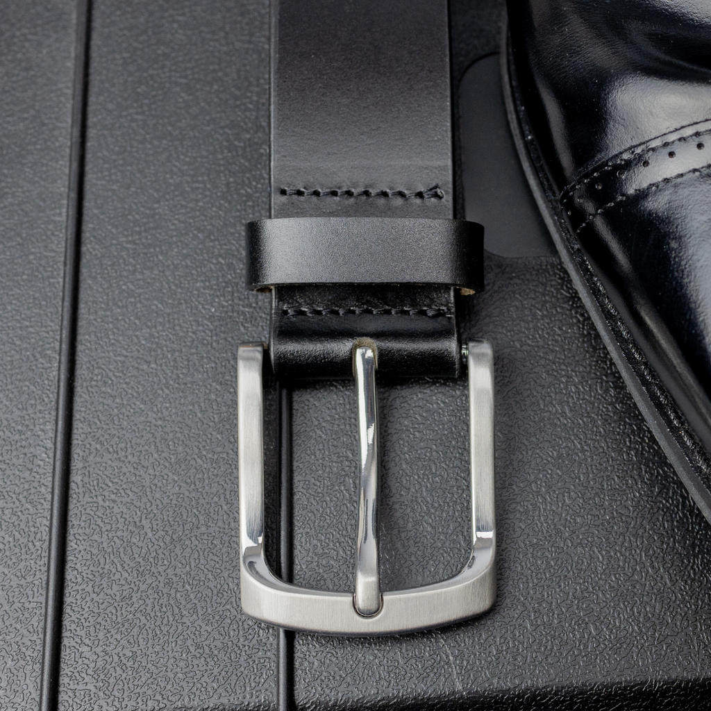 Nickel Free silver low profile curved buckle sewn onto black top grain leather strap next to a shoe.