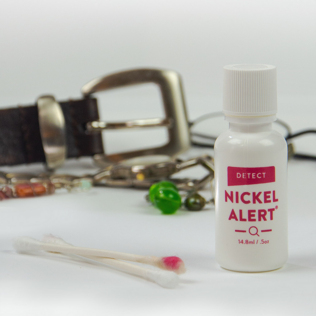 Image of Nickel Alert - nickel detection kit - with a cotton swab that has a pink color on it indicating a positive test for nickel in the items tested: belt buckle, earrings, eye glasses.